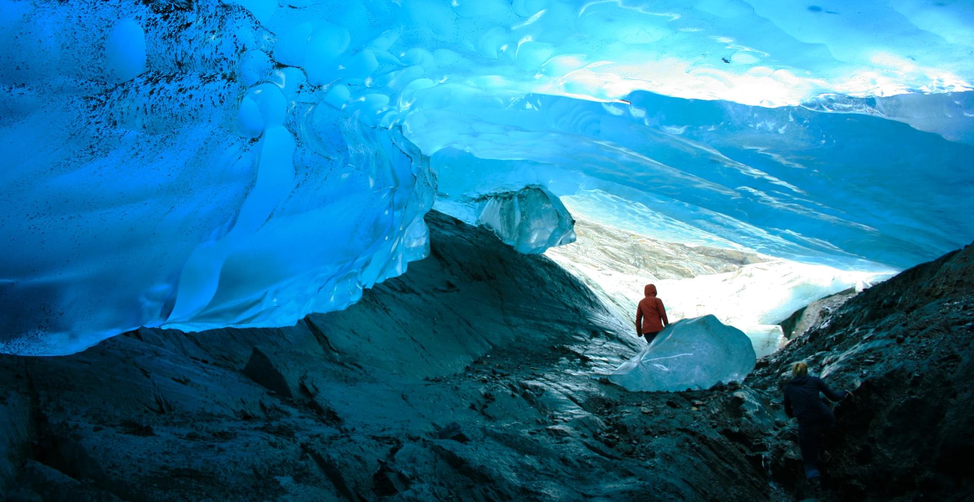 traveler walking under blue glacial ice in alaska